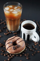 Caramel donut with coffee decoration next to a glass of iced frappuccino with a cup of black coffee on a dark background