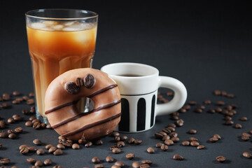 Caramel donut with coffee decoration next to a glass of iced frappuccino with a cup of black coffee on a dark background