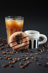 Caramel donut with coffee decoration next to a glass of iced frappuccino with a cup of black coffee on a dark background
