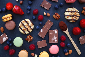 Macarons, chocolate, cookies, berries and various nuts on dark blue background. Top view.