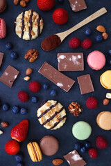 Macarons, chocolate, cookies, berries and various nuts on dark blue background. Top view.