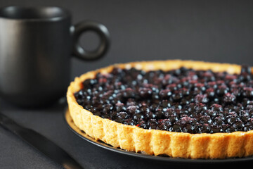 Blueberry pie next to a knife and a black cup on a dark background