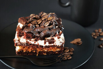Chocolate cake with coffee flavor on a black plate next to a cup of coffee on a dark background