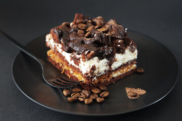 Chocolate cake with coffee flavor on a black plate next to a fork on a dark background