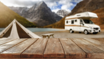 Wooden table in the tent and blurred motorhome at sunset in the mountain near the lake. Cool and relaxing concept. For product display montage or key visual layout design. space for text
