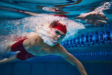 Powerful strokes pf swimmer developing speed. Young swimming male athlete in motion, in cap and...