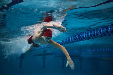 Freestyle stroke. Focused young man, swimmer in motion in swimming pool, training. Athleticism and...