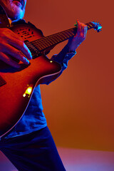 Cropped photo of mature man guitarist performing chords of rock-ballad in colorful neon light...