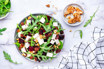 Beetroot and white cheese salad with arugula, lettuce, chard and walnuts, white table, copy space. Fresh useful vegetarian dish for healthy eating