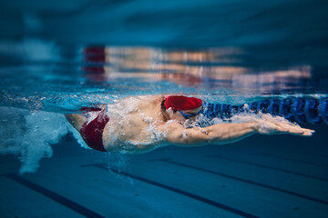 Muscular young man, swimmer in motion, preparing for competition, training in swimming pool indoors. Speed and technique. Concept of professional sport, health, endurance, strength, active lifestyle - obrazy, fototapety, plakaty