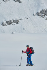 A female skier stands at the snowy summit of a mountain, equipped with professional gear and skis,...