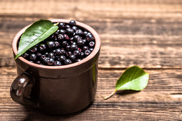 Chokeberry. Bowl of fresh aronia berries with leaves on wooden table. - 783082071