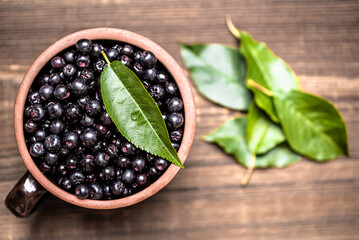 Chokeberry. Bowl of fresh aronia berries with leaves on wooden table.