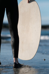 Junge im Neoprenanzug mit Skimboard in der Hand am Strand im Wasser am Meer auf Sardinien