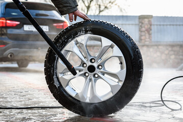 Man washing car's alloy wheels with high pressure washing.