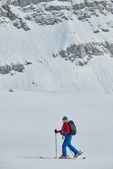 A female skier stands at the snowy summit of a mountain, equipped with professional gear and skis,...