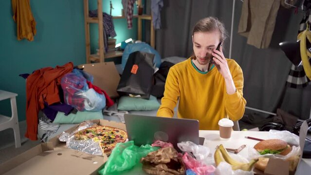 Teenager working studying in messy room. Student Calling on mobile phone, typing on laptop computer sitting in among garbage