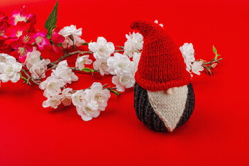 Minimalist spring greeting card with knitted gnome and blooming cherry branches