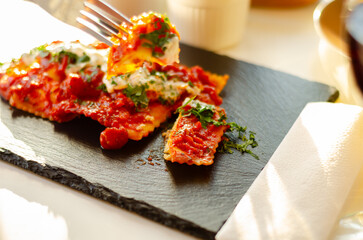 Four cheese filled ravioli in a tomato and basil sauce on the black stone plate - 783088074