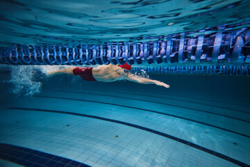 Power, concentration and resilience. Young athletic man, swimmer in motion, swimming freestyle in...