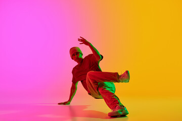 Fototapeta na wymiar Young athlete man, dressed urban style outfit dancing in motion in neon light against gradient pink-yellow background. Concept of hobby, sport, creativity, fashion and style, action. Ad
