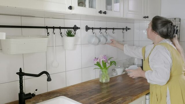 mature housewife in apron tidies up kitchen, washing countertop, showcasing routine household cleaning, Daily activities, Kitchen maintenance, Household chores, Domestic life