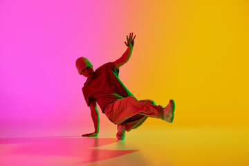 Dynamic photo of young, stylish dressed man performing in neon light against gradient pink-yellow...