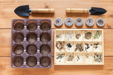 Spring sowing work in the garden. Top view of a set of different vegetable and flower seeds in a wooden box and peat tablets in a container for growing seedlings. Flat lay, close-up, top view