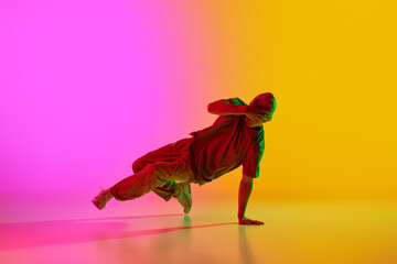 Cool attitude young man performing breakdance in motion in neon light against gradient pink-yellow...