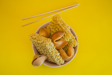 A bowl with dried noodles, fortune cookies and chopsticks on yellow background. Flat lay. - 783101443