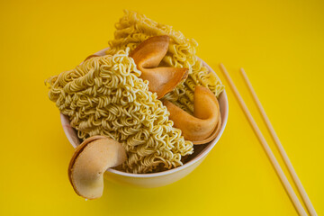A dried noodles, fortune cookies and chopsticks in a bowl on yellow background. - 783101485