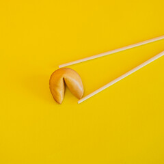Chopsticks hold a fortune cookie on yellow background. Flat lay, top view.
