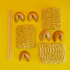 A fortune cookies, dried noodles and chopsticks are laid out on yellow background, flat lay, top view