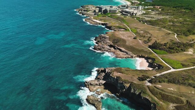 Aerial view of Caribbean Sea's tropical rocky coastline features waves colliding with rocks amid untamed surroundings, bathed in brilliant sunlight and embraced by turquoise waters
