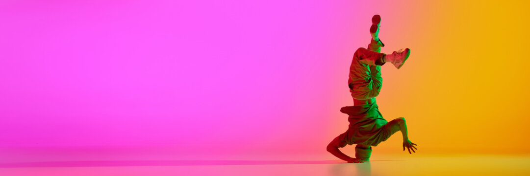 Banner. Break-dancer spinning on head in motion in neon light against gradient pink-yellow background with negative space to insert text. Concept of art, hobby, sport, fashion and style, action. Ad