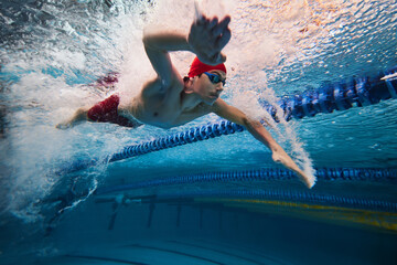 Water bubbles demonstrating speed. Young man, swimming athlete in motion in pool training, preparing for competition. Concept of professional sport, health, endurance, strength, active lifestyle - obrazy, fototapety, plakaty