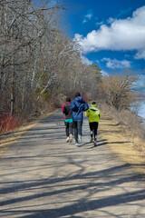 Rear view of three joggers running on a forest trail next to a river, daytime, sunny