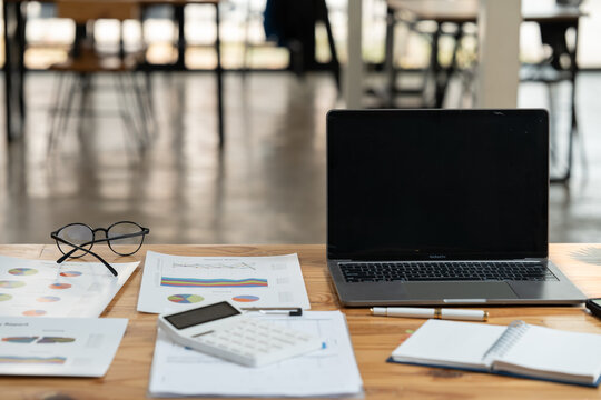 Office desk showcasing financial reports, pie charts, and graphs on paper next to a laptop, calculator, glasses, and notebook, representing data analysis and business planning