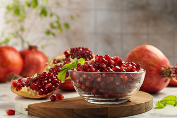 Ripe juicy pomegranate grains in bowl and green leaves on white table