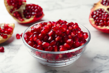 Ripe juicy pomegranate grains in bowl on white marble table