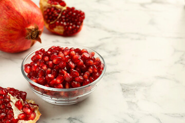 Ripe juicy pomegranate grains in bowl on white marble table, space for text