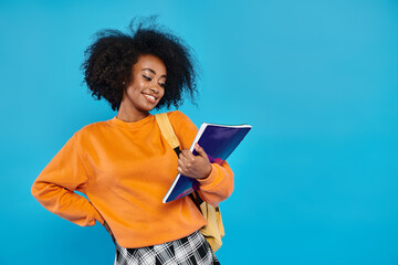 African American college girl in orange shirt holding a book, exuding knowledge and inspiration in...