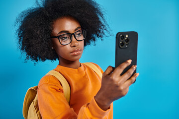 An African American college girl in casual attire, wearing glasses, taking a selfie with her cell...