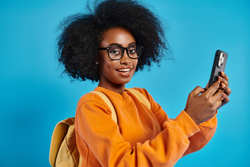 An African American college girl in casual attire, wearing glasses, holding a cell phone in a...