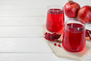Tasty pomegranate juice in glasses and fresh fruits on white wooden table, closeup. Space for text