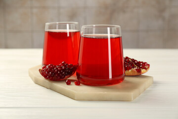 Tasty pomegranate juice in glasses and fresh fruit on white wooden table