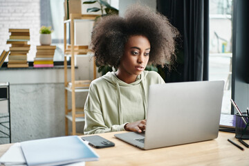 A multicultural woman engrossed in work, seated in front of her laptop computer in a modern coworking space.