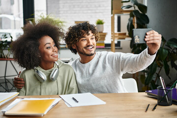 A man and woman capture a moment, smiling together while taking a selfie in a modern office setting.