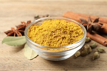 Curry powder in bowl and other spices on wooden table, closeup