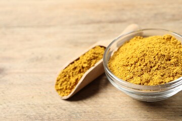 Curry powder in bowl and scoop on wooden table, closeup. Space for text